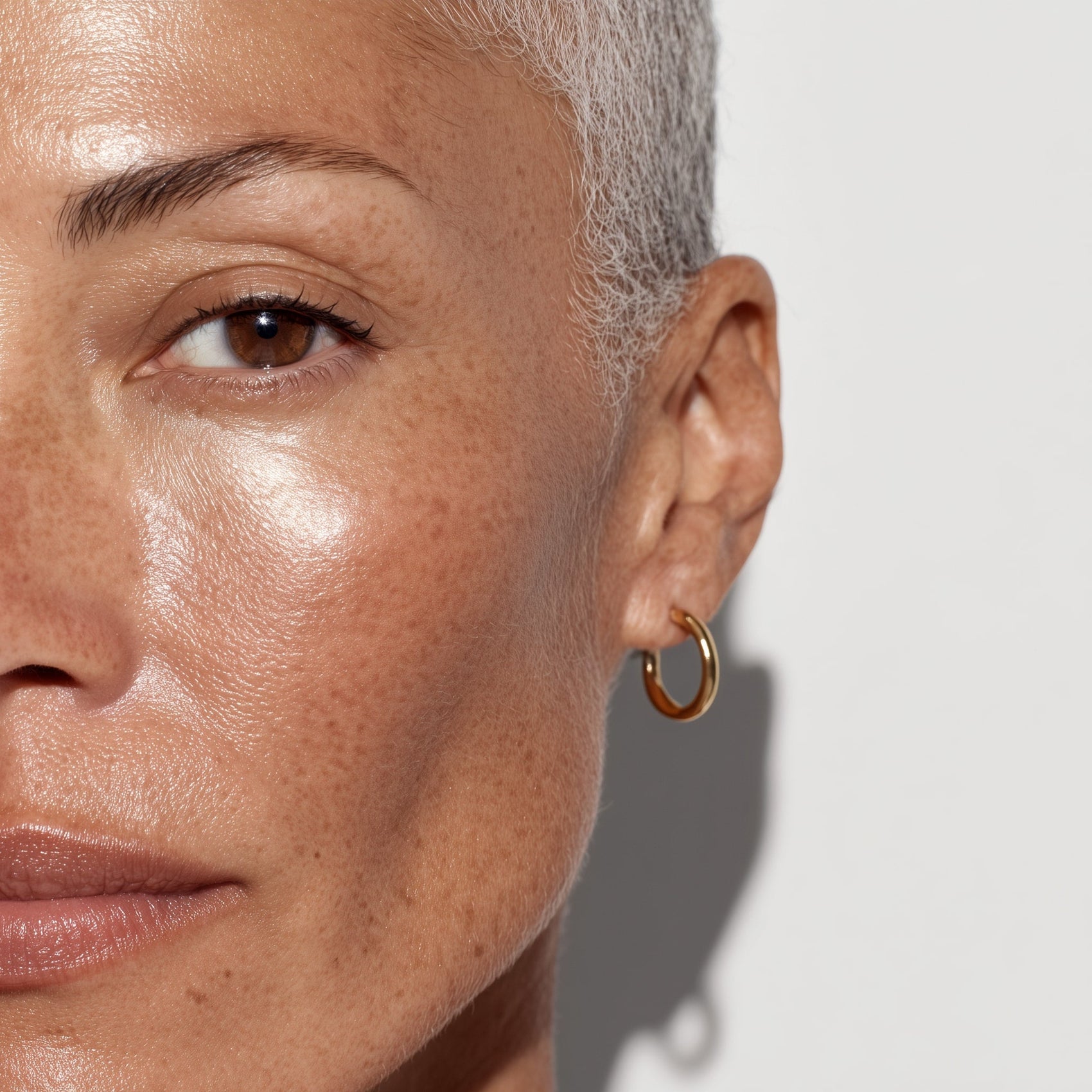 Close-up of a person's face with a gold hoop earring on a neutral background (Beige)