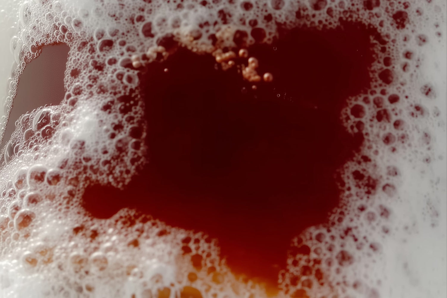 Close-up of a heart-shaped foam pattern on a red liquid background