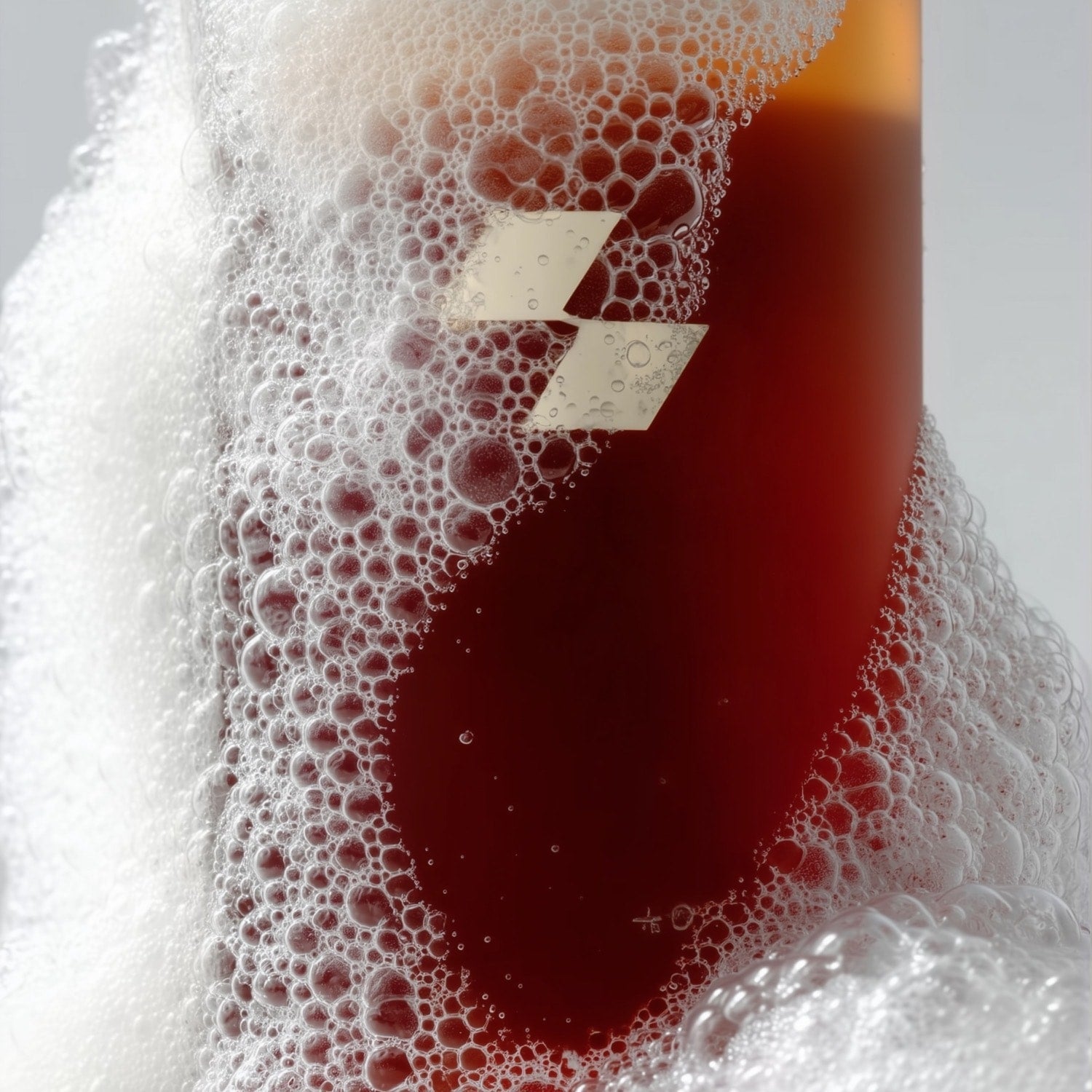 Close-up of a glass filled with a dark liquid and foam, with a brand label visible.