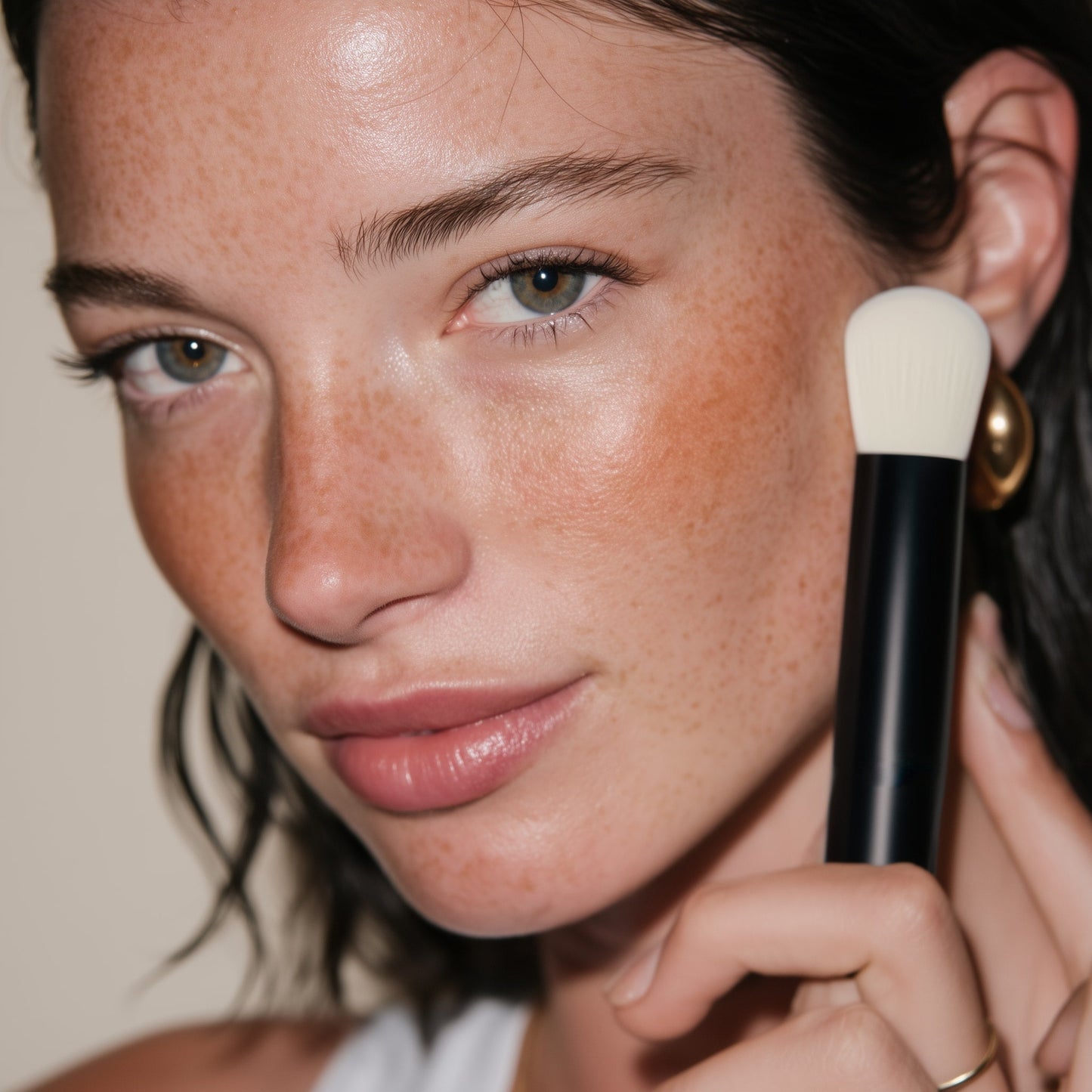 Woman holding a makeup brush near her face with a neutral background