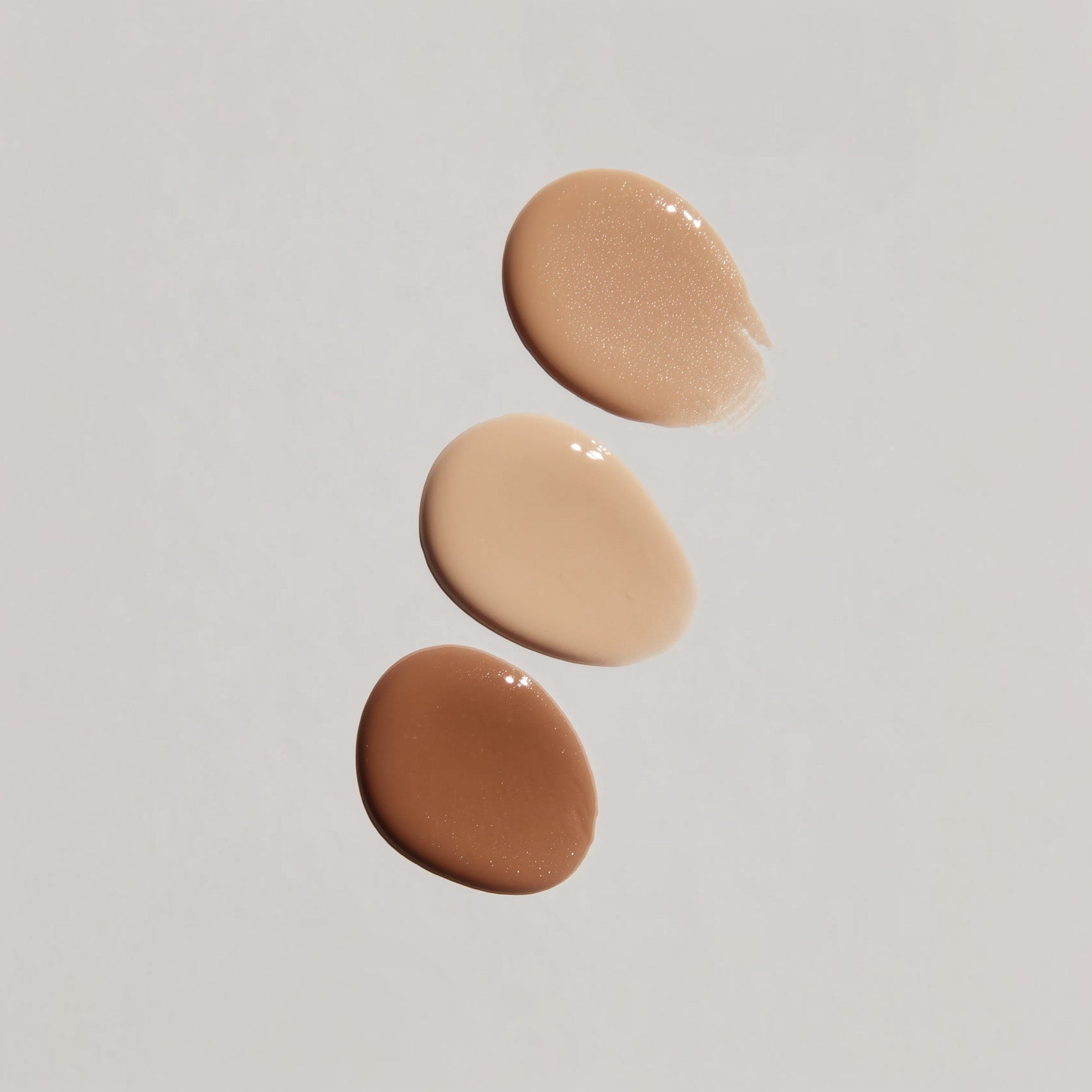 Three swatches of different tones of beige cream on a light gray background