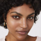 Close-up of a woman with short curly hair and gold earrings against a neutral background (Medium beige)