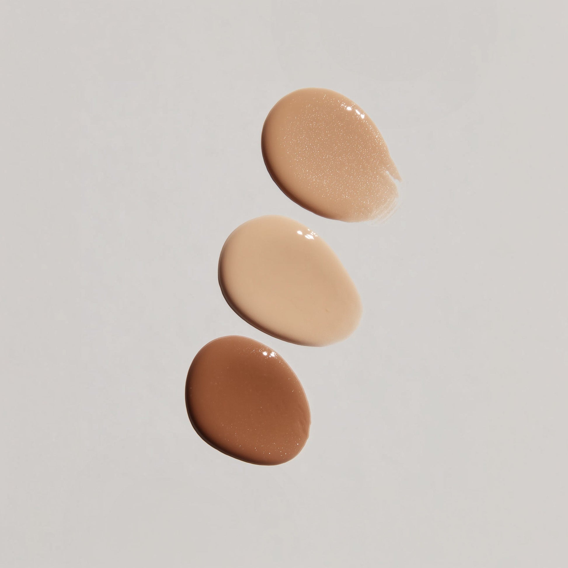 Three swatches of different tones of beige cream on a light gray background