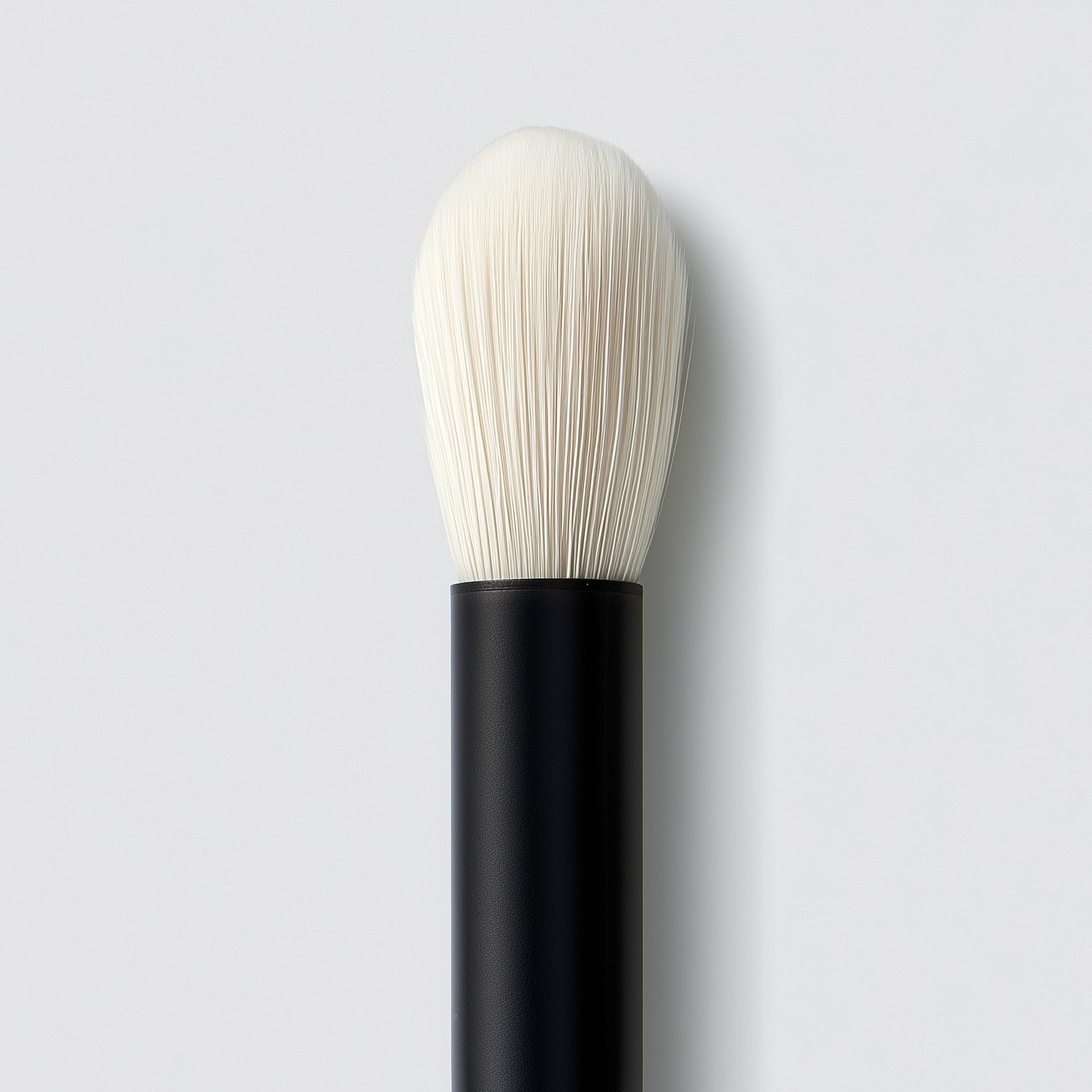 Makeup brush with black handle and white bristles on a light gray background