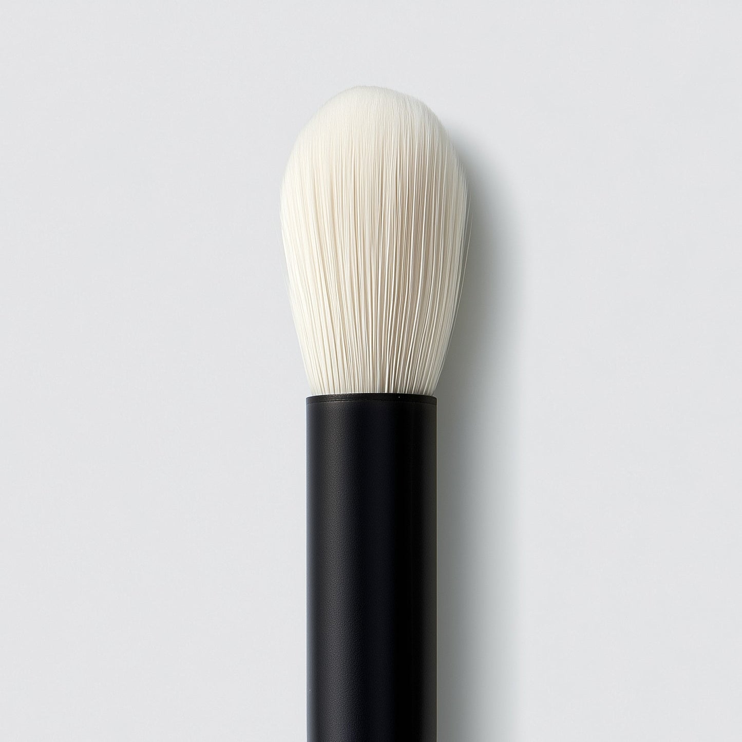 Makeup brush with black handle and white bristles on a light gray background