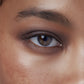 Close-up of a person's eye with brown iris and eyelashes.