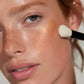 Close-up of a person applying makeup with a brush to their face.