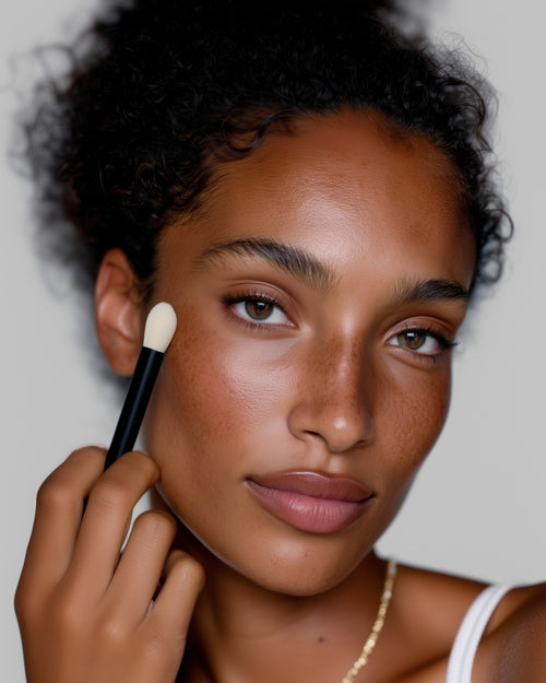 Woman applying makeup with a brush on a neutral background