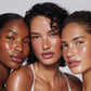 Three women with natural makeup and skin tones posing together against a neutral background.