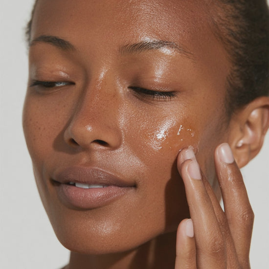 Close-up portrait of a person gently applying a translucent facial serum to their cheek with their fingers.
