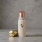 Shimmering cream highlighter stick in a white and gold tube with the cap placed beside it.
