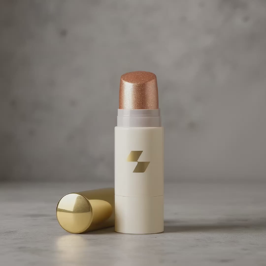 Shimmering cream highlighter stick in a white and gold tube with the cap placed beside it.