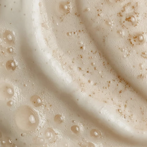 Close-up of a creamy skincare texture with visible droplets and fine exfoliating particles.