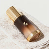 Amber-toned skincare bottle with a metallic gold cap placed on a neatly folded white towel.