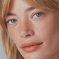 Close-up portrait of a person with freckles wearing soft peach-toned makeup.