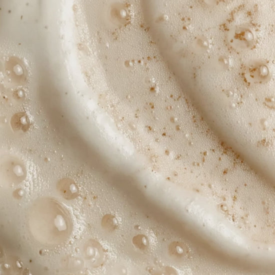 Close-up of a creamy skincare texture with visible droplets and fine exfoliating particles.