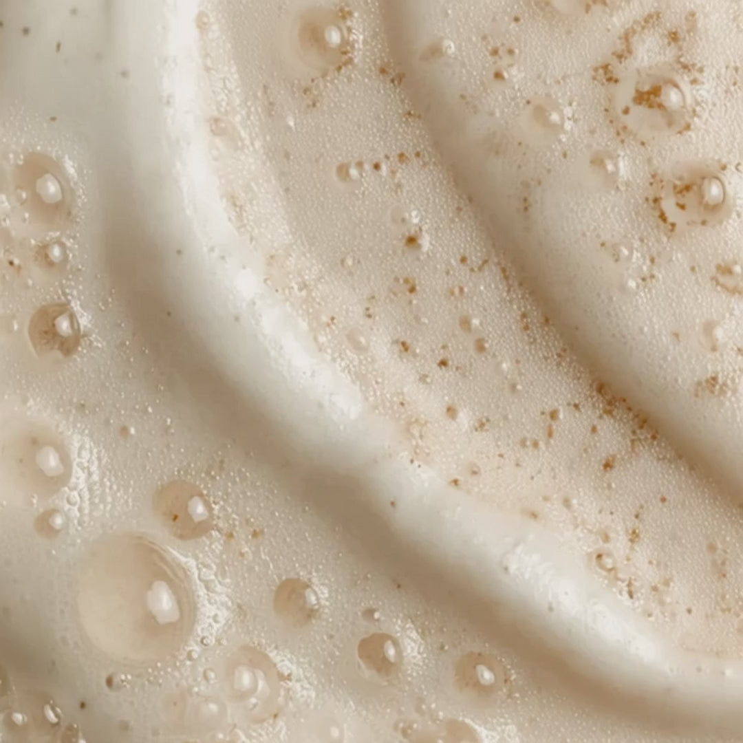 Close-up of a creamy skincare texture with visible droplets and fine exfoliating particles.