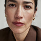Close-up of a woman with short hair wearing gold earrings against a neutral background (Rich Red)