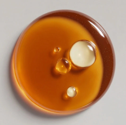Close-up of a round amber-colored object with three droplets on a light gray background