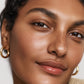 Close-up of a woman's face with gold hoop earrings on a neutral background (Pink)