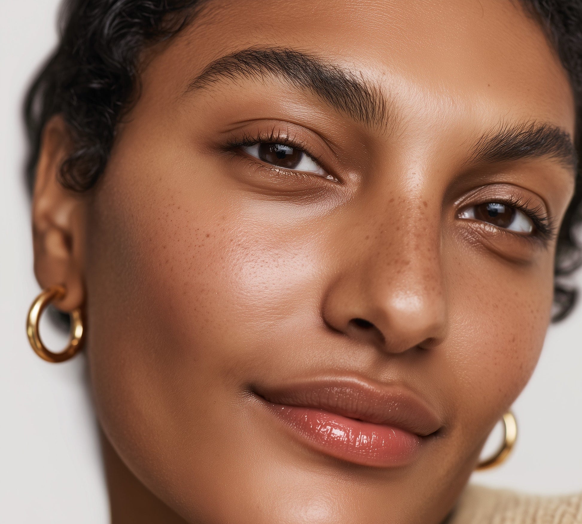 Close-up of a woman's face with gold hoop earrings on a neutral background (Pink)