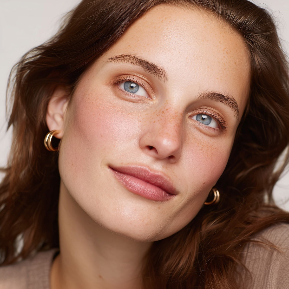 Close-up of a woman with blue eyes and freckles, wearing gold earrings (Pink)