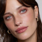 Close-up of a woman's face with gold earrings on a neutral background (Marsala)